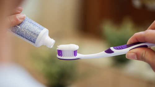 Hands squeezing white toothpaste from a tube onto a purple toothbrush
